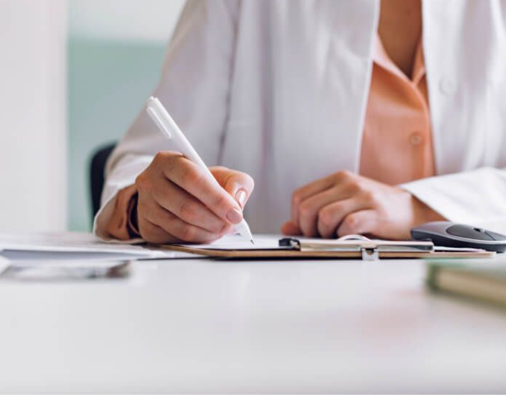 Healthcare professional writing a referral or medical note on a clipboard.