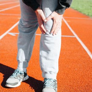 Person clutching their knee on a running track, indicating pain or injury.