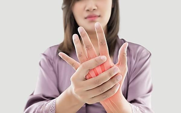 Woman holding her right hand in pain, highlighting joint discomfort in the palm and fingers.