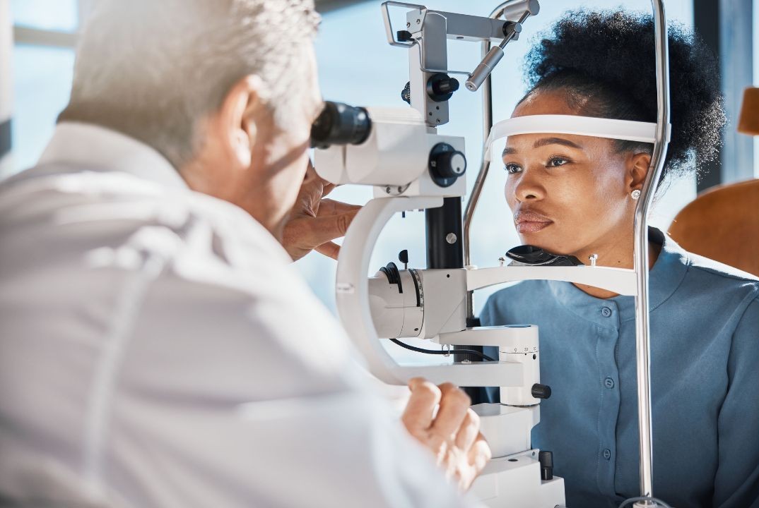 Female patient undergoing a slit-lamp eye examination by an ophthalmologist, seated in a modern clinical setting.